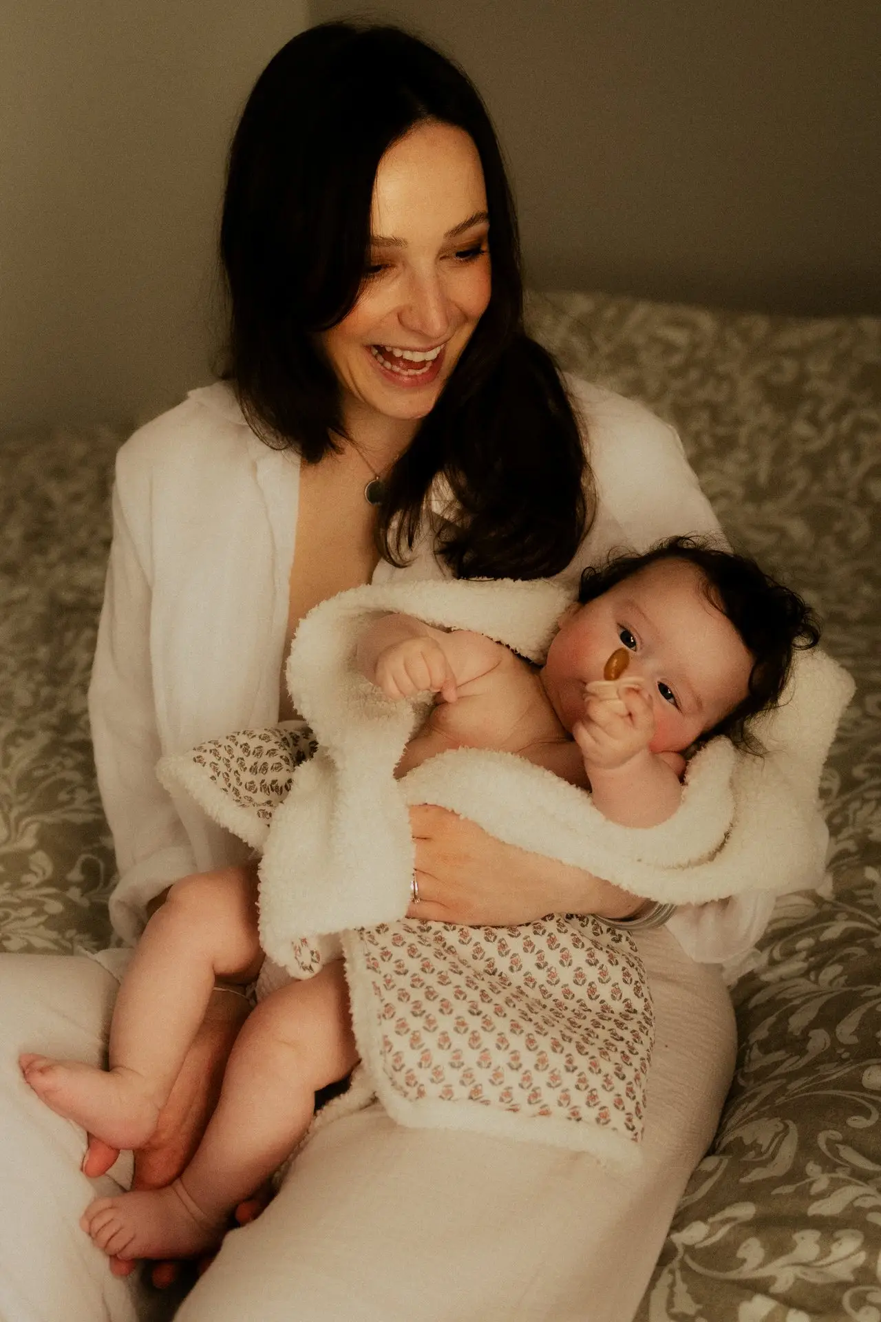 Maman souriante tenant son nouveau-né en peau à peau lors d'une séance naissance en studio - Melissa Jai Photographe