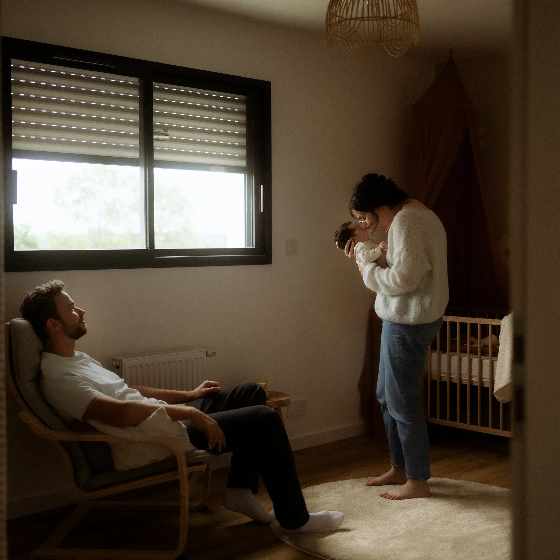 Parents avec leur nouveau-né dans la chambre de bébé lors d'une séance naissance à domicile - Melissa Jai Photographe