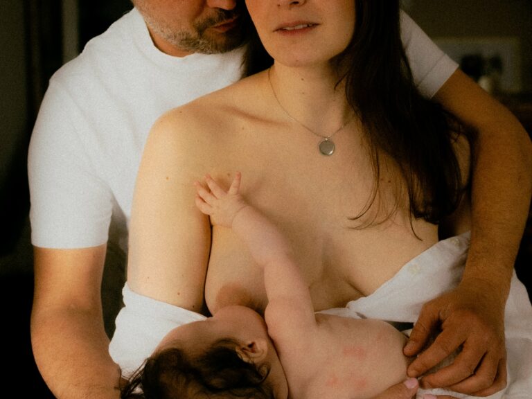 Papa enlacant maman qui allaite leur bébé en cadrage serré intimiste avec collier pendentif lors d'une séance photo allaitement en couple