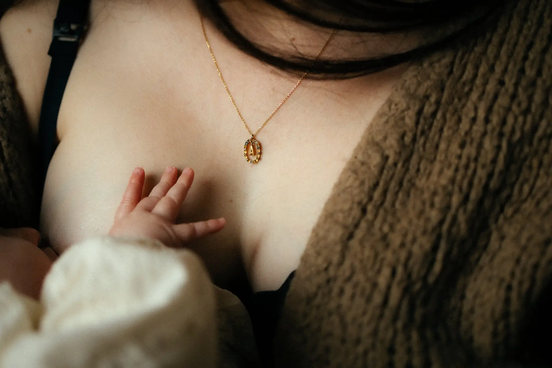 Détail d'un bébé au sein avec collier doré de maman lors d'une séance allaitement en studio - Melissa Jai Photographe