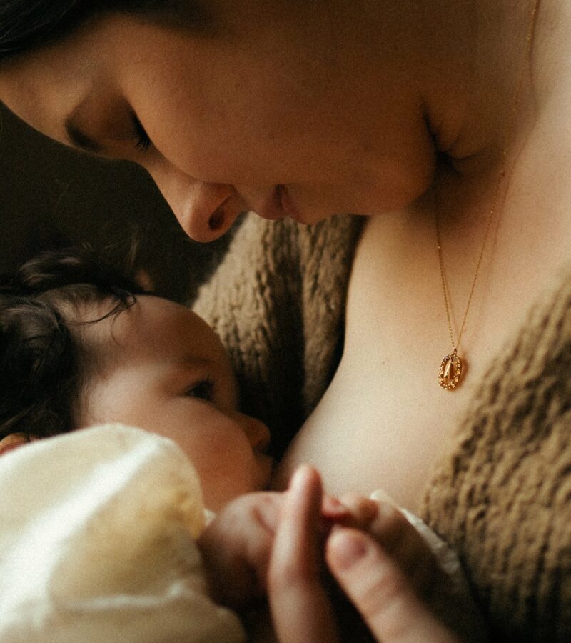 Detail allaitement bebe en gros plan avec collier dore en lumiere chaude et douce - Melissa Jai Photographe