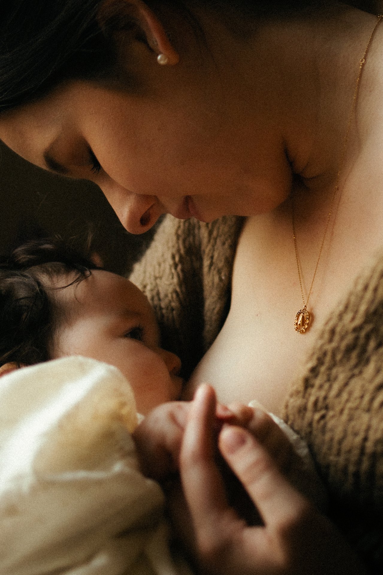Detail allaitement bebe en gros plan avec collier dore en lumiere chaude et douce - Melissa Jai Photographe