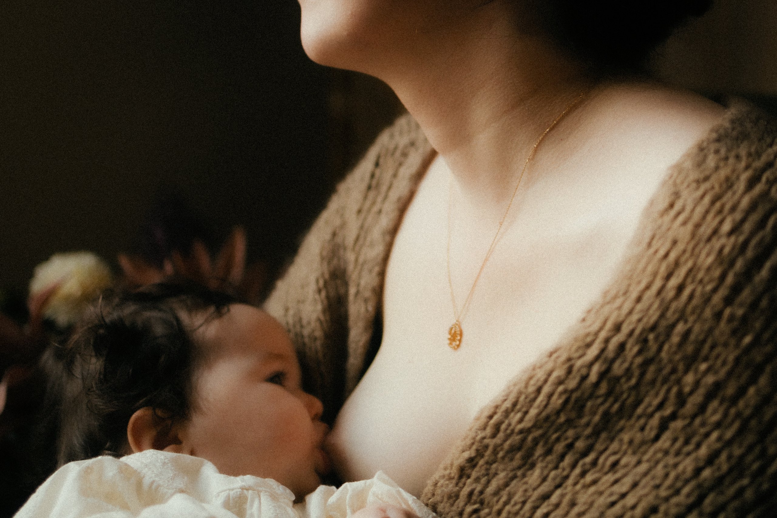 Maman allaitant son bebe avec un collier en or dans une lumiere douce et intimiste - Melissa Jai Photographe