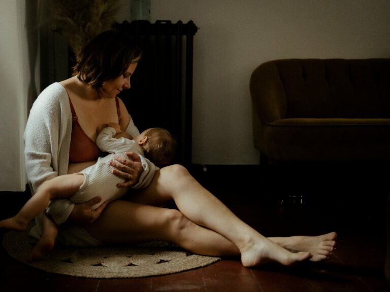 Maman assise au sol sur un tapis en jute allaitant son bébé en gilet beige dans une ambiance intime à domicile lors d'une séance photo allaitement