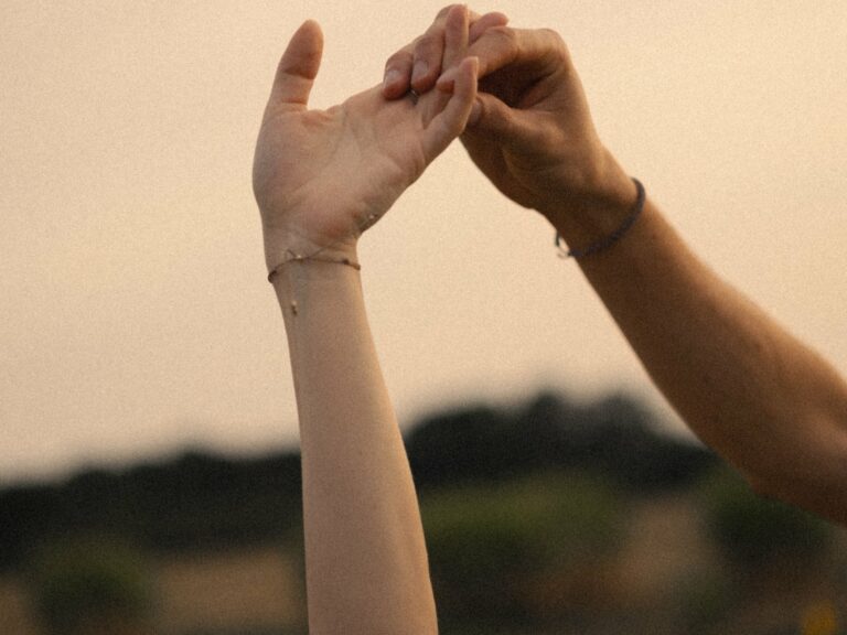 Deux mains entrelacées levées vers le ciel doré au coucher du soleil avec bracelets lors d'une séance photo couple en extérieur golden hour