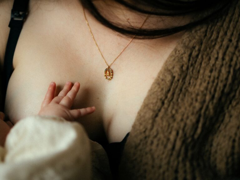 Detail seance naissance petite main de bebe sur poitrine maman avec collier dore photographe Melissa Jai
