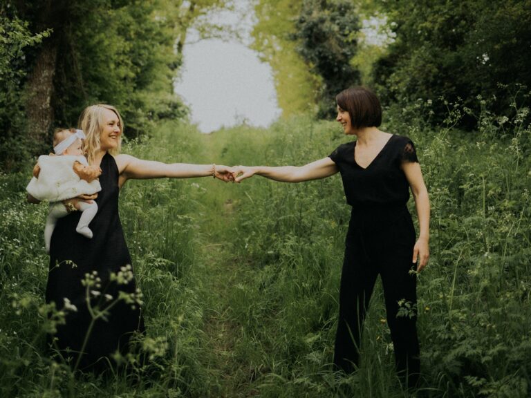 Deux mamans se tenant la main sur un chemin verdoyant en nature avec leur bébé lors d'une séance photo famille en extérieur