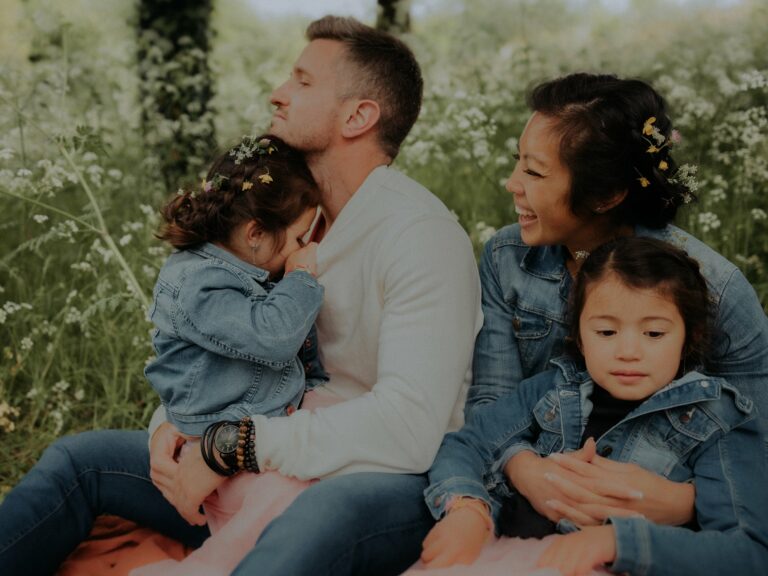 Famille avec papa maman et deux petites filles en vestes jean avec fleurs dans les cheveux assise dans un champ fleuri lors d'une séance photo famille en extérieur nature