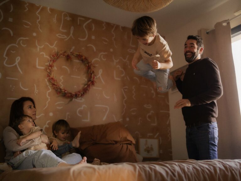 Papa faisant sauter son enfant sur le lit pendant que maman câline les deux autres enfants lors d'une séance photo famille à domicile