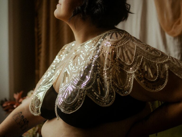 Femme enceinte portant un châle en dentelle dorée à sequins lors d'une séance photo grossesse boudoir intime en lumière naturelle