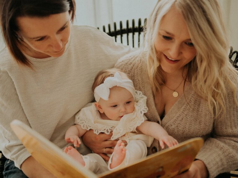 Deux mamans lisant un livre à leur bébé portant un bandeau blanc et une robe en dentelle en gros plan lors d'une séance photo famille en studio lumineux