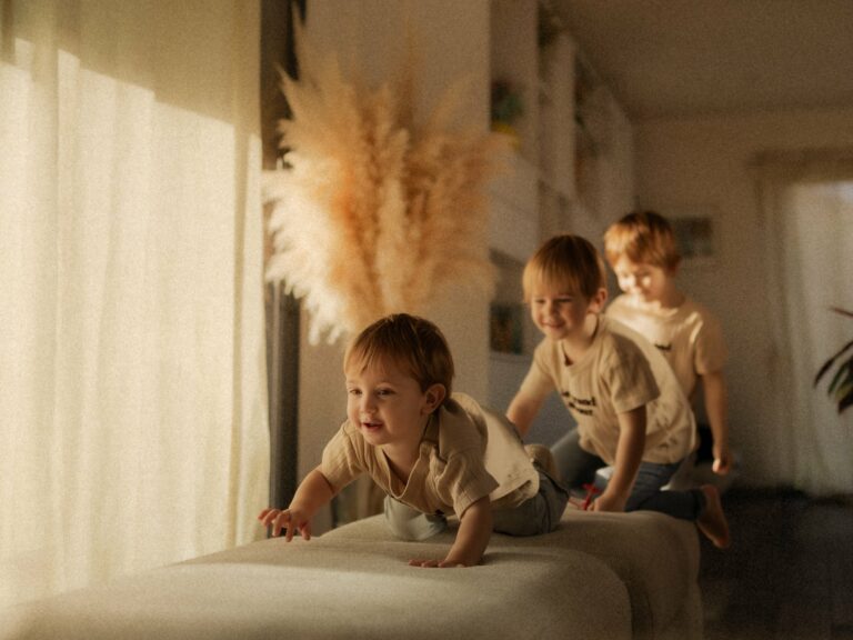 Trois jeunes enfants jouant et grimpant sur un canapé en studio photo avec herbes de pampa et lumière naturelle douce lors d'une séance famille