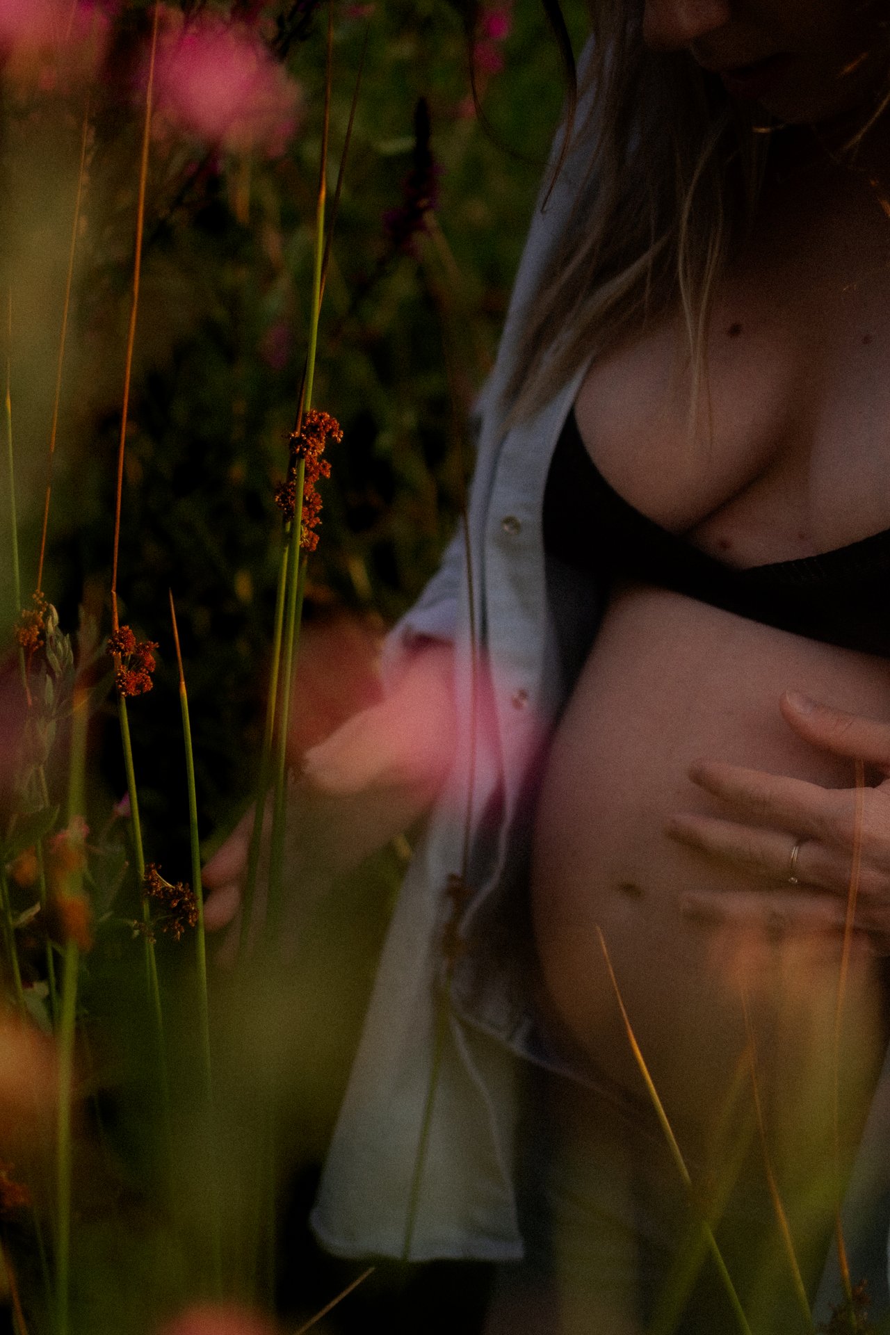 Detail de fleurs sauvages roses avec ventre de femme enceinte en arriere-plan lors d'une seance grossesse en exterieur - Melissa Jai Photographe
