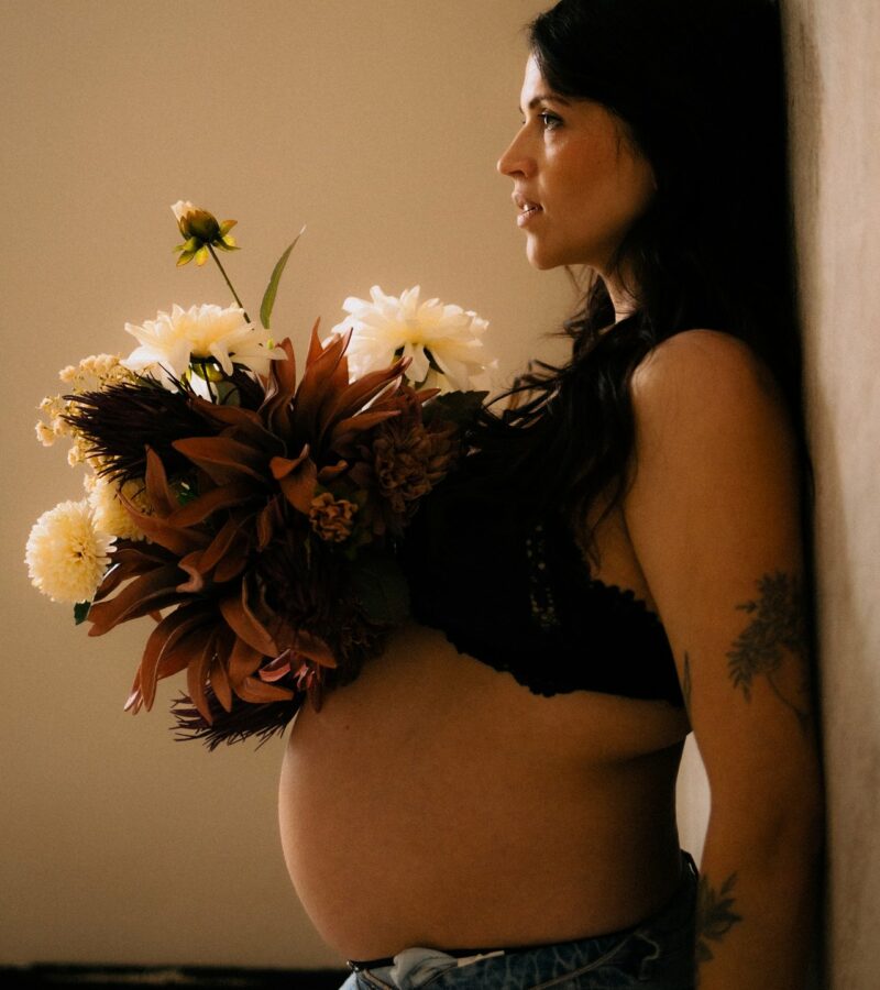 Femme enceinte de profil tenant un bouquet de fleurs lors d'une seance grossesse en studio - Melissa Jai Photographe
