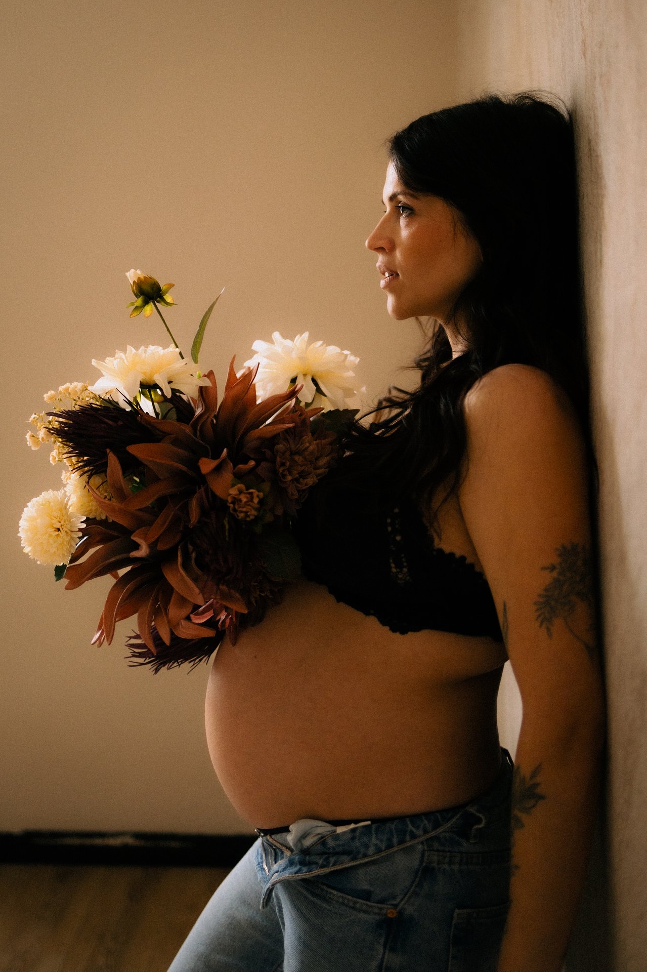 Femme enceinte de profil tenant un bouquet de fleurs lors d'une seance grossesse en studio - Melissa Jai Photographe