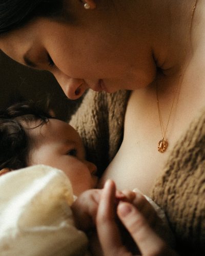 Detail allaitement bebe en gros plan avec collier dore en lumiere chaude et douce - Melissa Jai Photographe