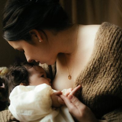 Gros plan allaitement maman allaitant bebe avec collier dore lumiere chaude photographe Melissa Jai