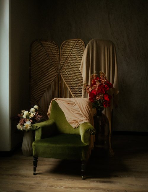 Decor de studio photo avec fauteuil en velours vert, bouquets de fleurs et paravent en rotin - Melissa Jai Photographe