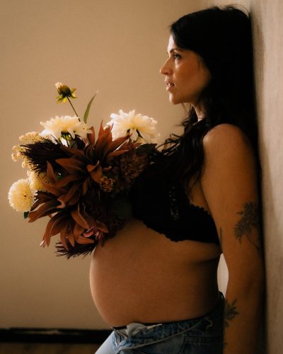 Femme enceinte de profil tenant un bouquet de fleurs lors d'une seance grossesse en studio - Melissa Jai Photographe